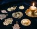 Quelques amulettes et talismans anciens en metal patine disposes sur un velours bleu nuit, bougie allumee, tons or