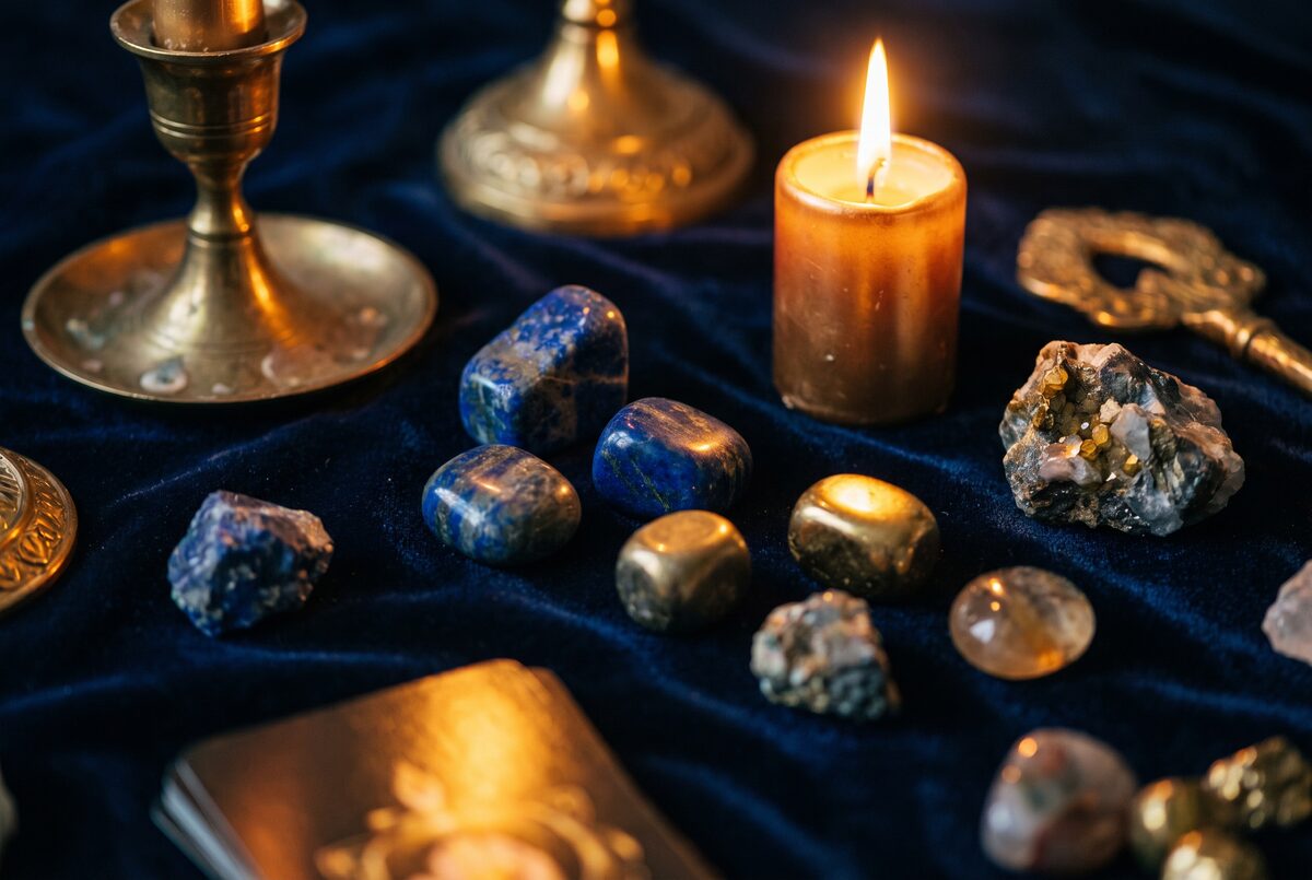 Pierres roulees et brutes disposees sur un velours bleu nuit a la lueur d une bougie, tons mineraux et or