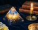 Une pyramide d'orgonite posée près d'une bougie, dans une ambiance feutrée bleu nuit et or